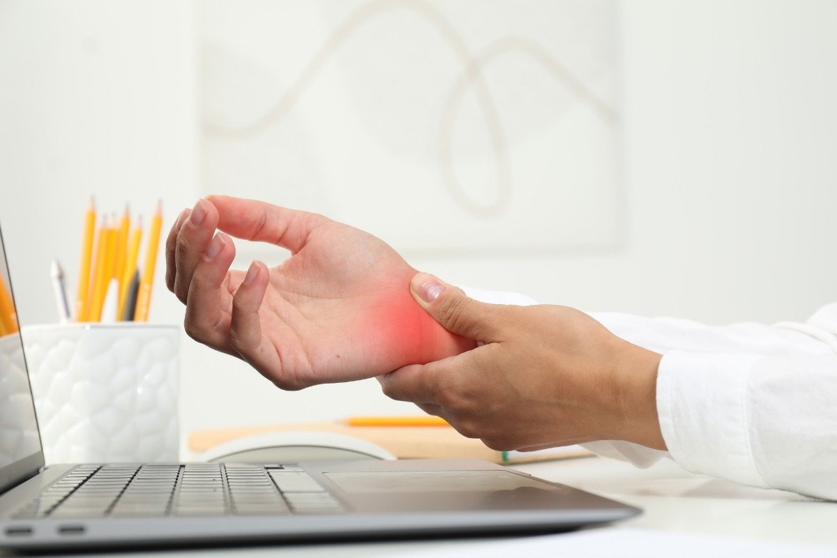 Person holding their wrist in pain while working at a laptop, a typical presentation of carpal tunnel syndrome