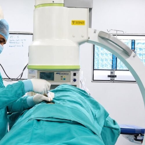 Surgical team at Sama Hospital, South Delhi, performing an image-guided minimally invasive spine procedure using a C-arm fluoroscope in the operating theatre
