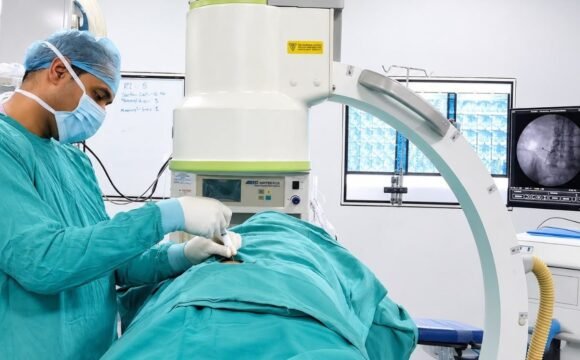 Surgical team at Sama Hospital, South Delhi, performing an image-guided minimally invasive spine procedure using a C-arm fluoroscope in the operating theatre